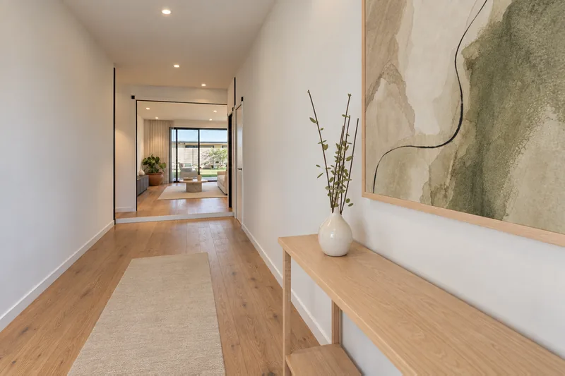 The entry gallery with a timber console and artwork, looking through to the living room