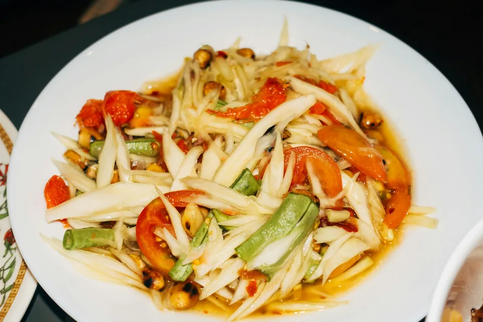 Green papaya som tam with snake bean, tomato and peanuts in a white bowl