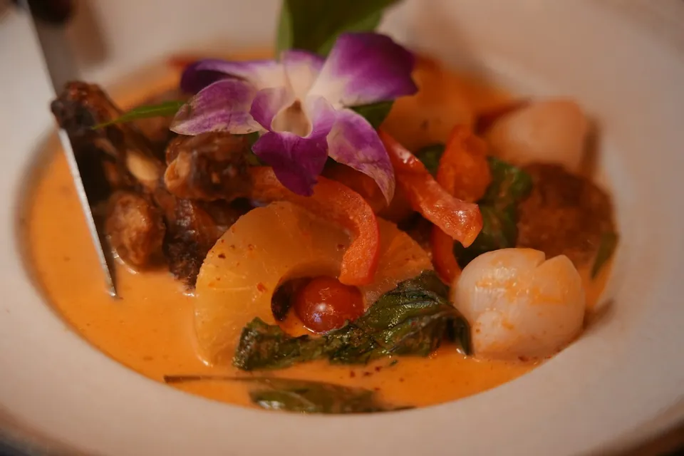 Red curry with roast meat, pineapple, lychee and cherry tomato, garnished with an orchid