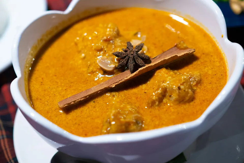 Massaman curry with a cinnamon stick, star anise and peanuts in a white bowl