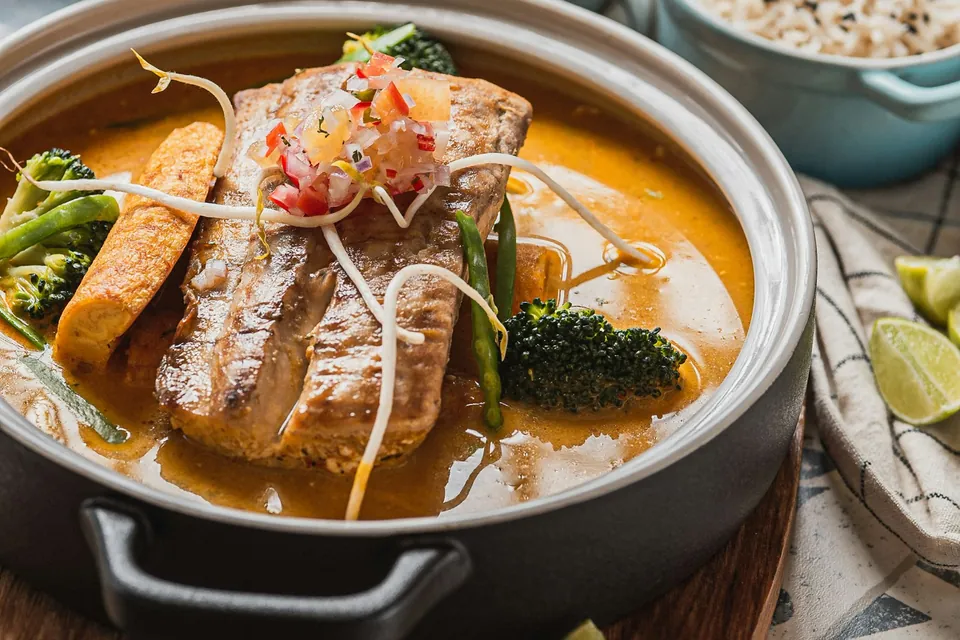 Yellow curry with a grilled fish fillet, green beans and bean sprouts in a stoneware pot