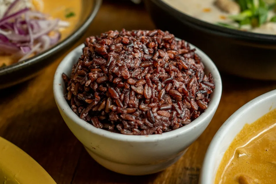 A small bowl of dark riceberry rice among shared dishes